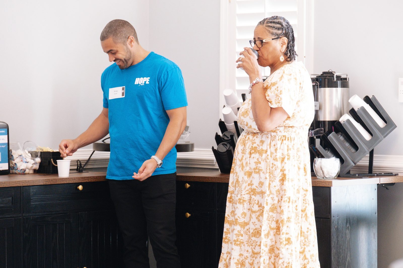 A Café Team volunteer in a HOPE shirt smiling at a guest holding her coffee