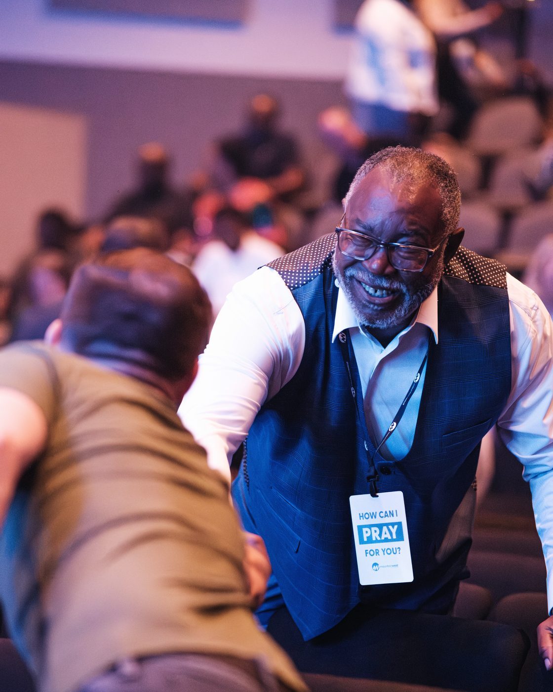 A Prayer Partner wearing a How can I pray for you? lanyard laughing as he greets someone