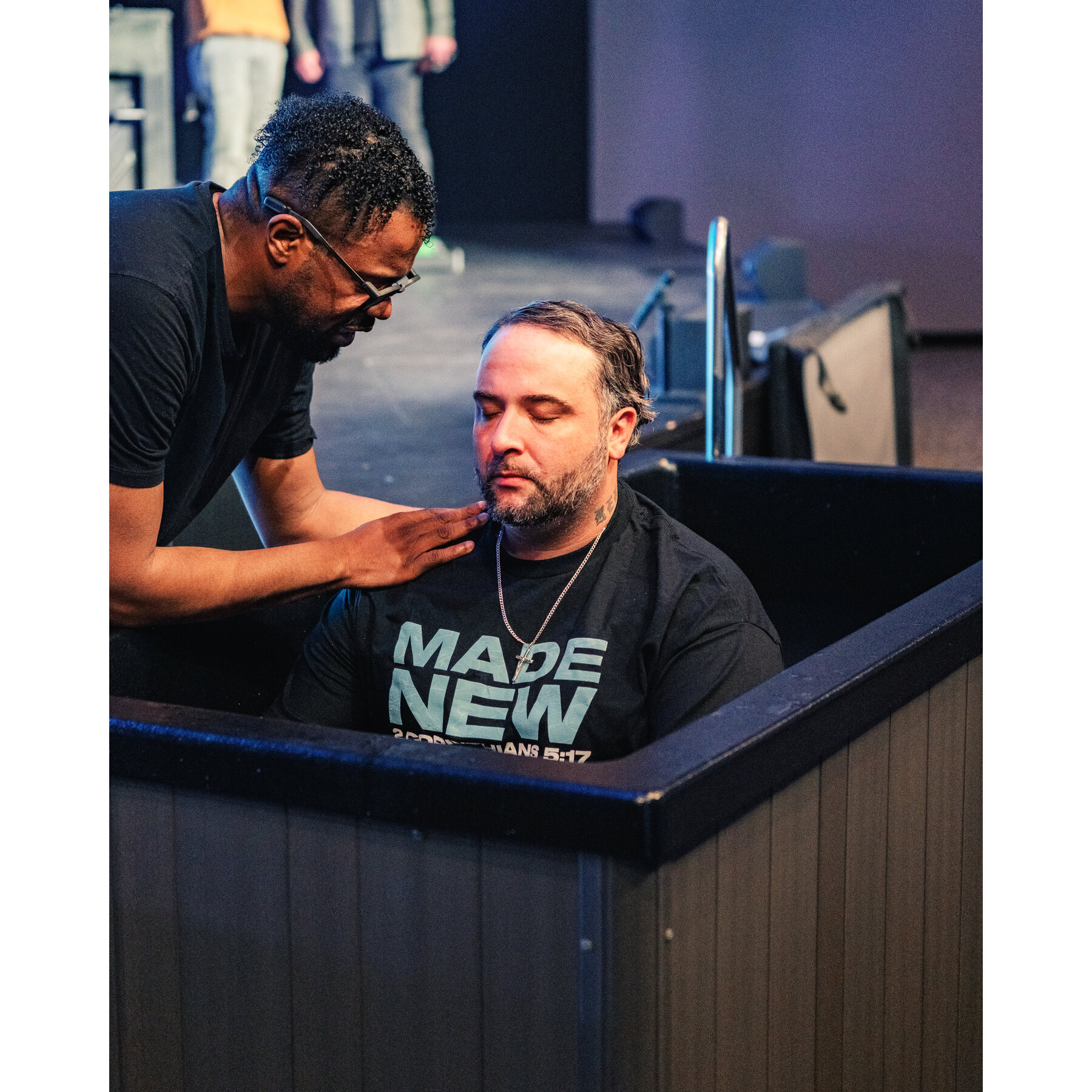 A pastor with a steadying hand under a man’s chin in the baptism tank, the moment before he goes under