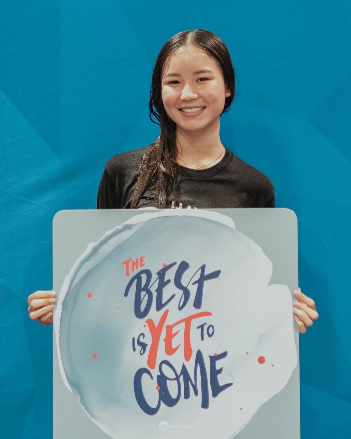 A young woman holding a sign reading The best is yet to come