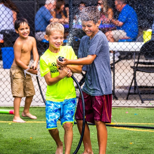 Two young boys spraying a hose together outside