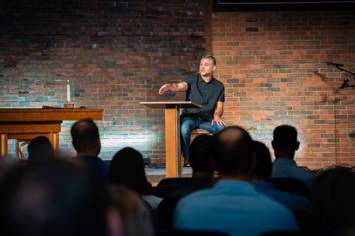 Pastor Andrew preaching in the Worship Center with a screen behind him