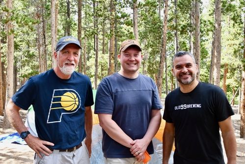 Three men smiling at the camera in the mountains together