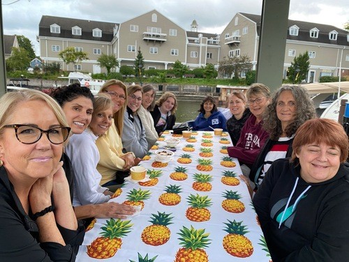 Picture of 12  women sitting around a table enjoying time together by the canal in Fairport.