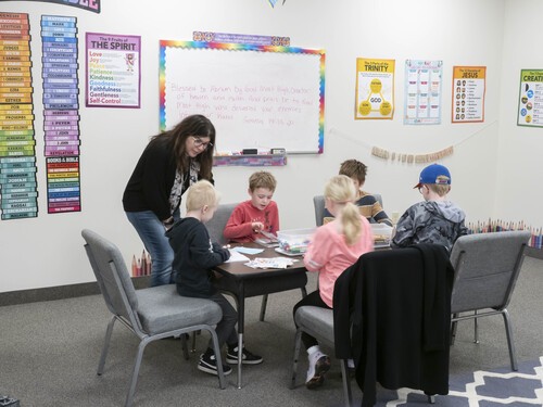 Picture of 5 students in Kidzone with their teacher, sitting around a table working on a craft project. 