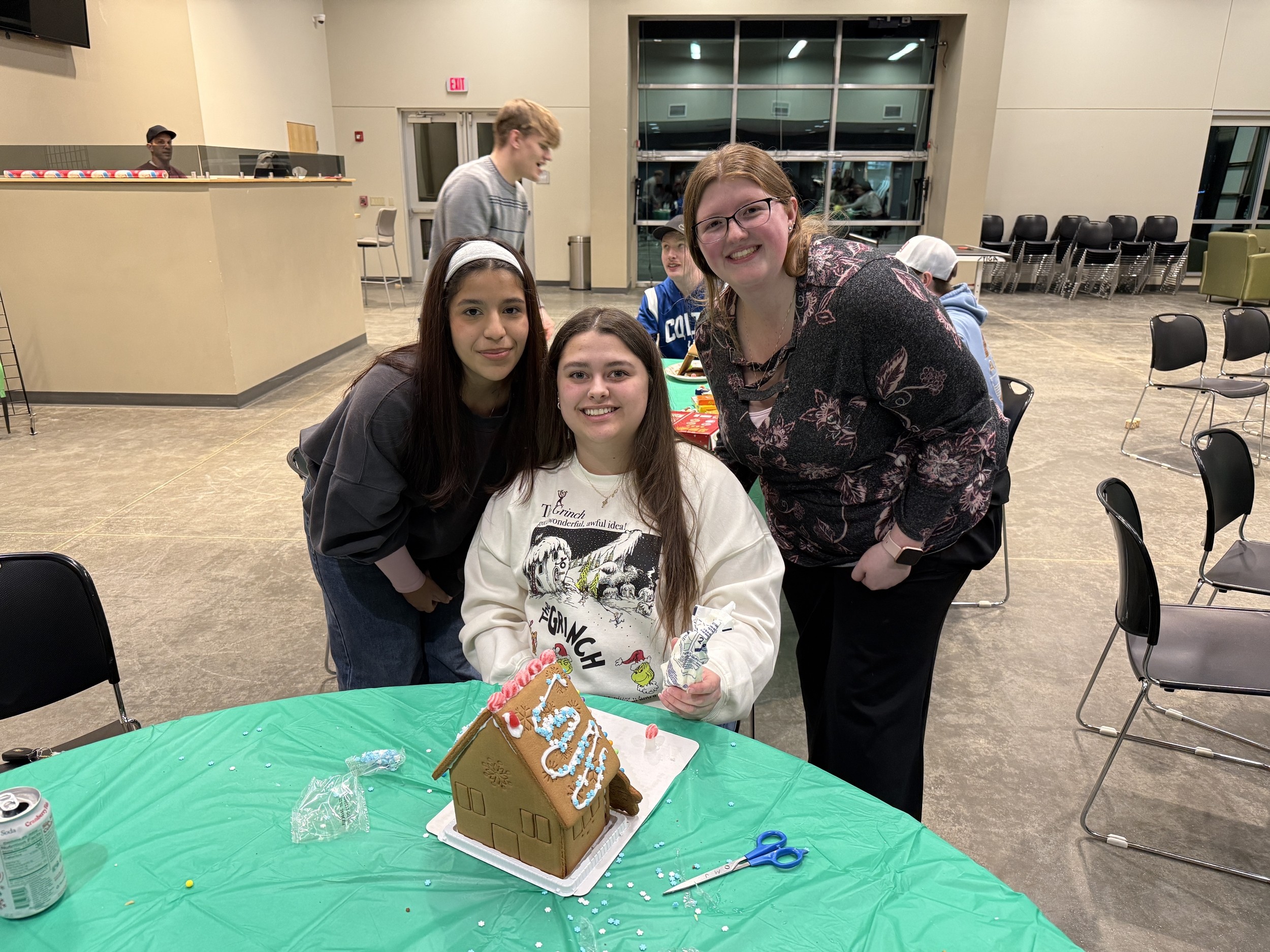 Young adults smiling around a gingerbread house table