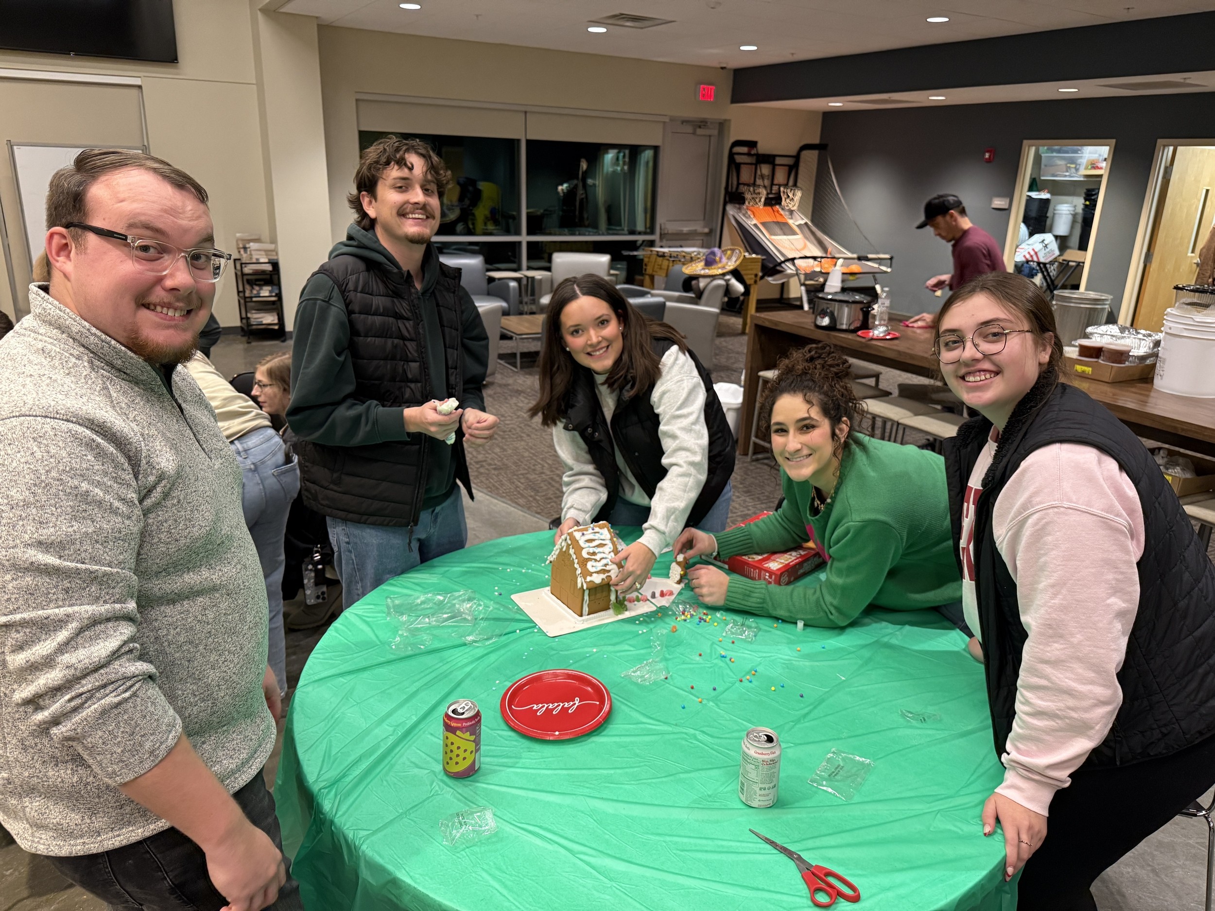 Young adults gathering around a gingerbread house activity